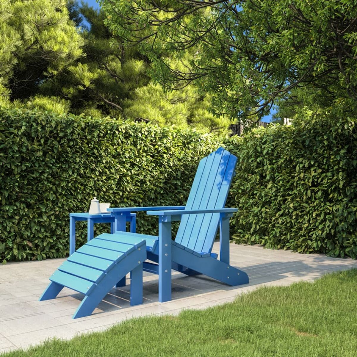 Blauer Stuhl und Fußstütze auf einer Terrasse, grüne Hecke dahinter, unter Bäumen an einem sonnigen Tag.