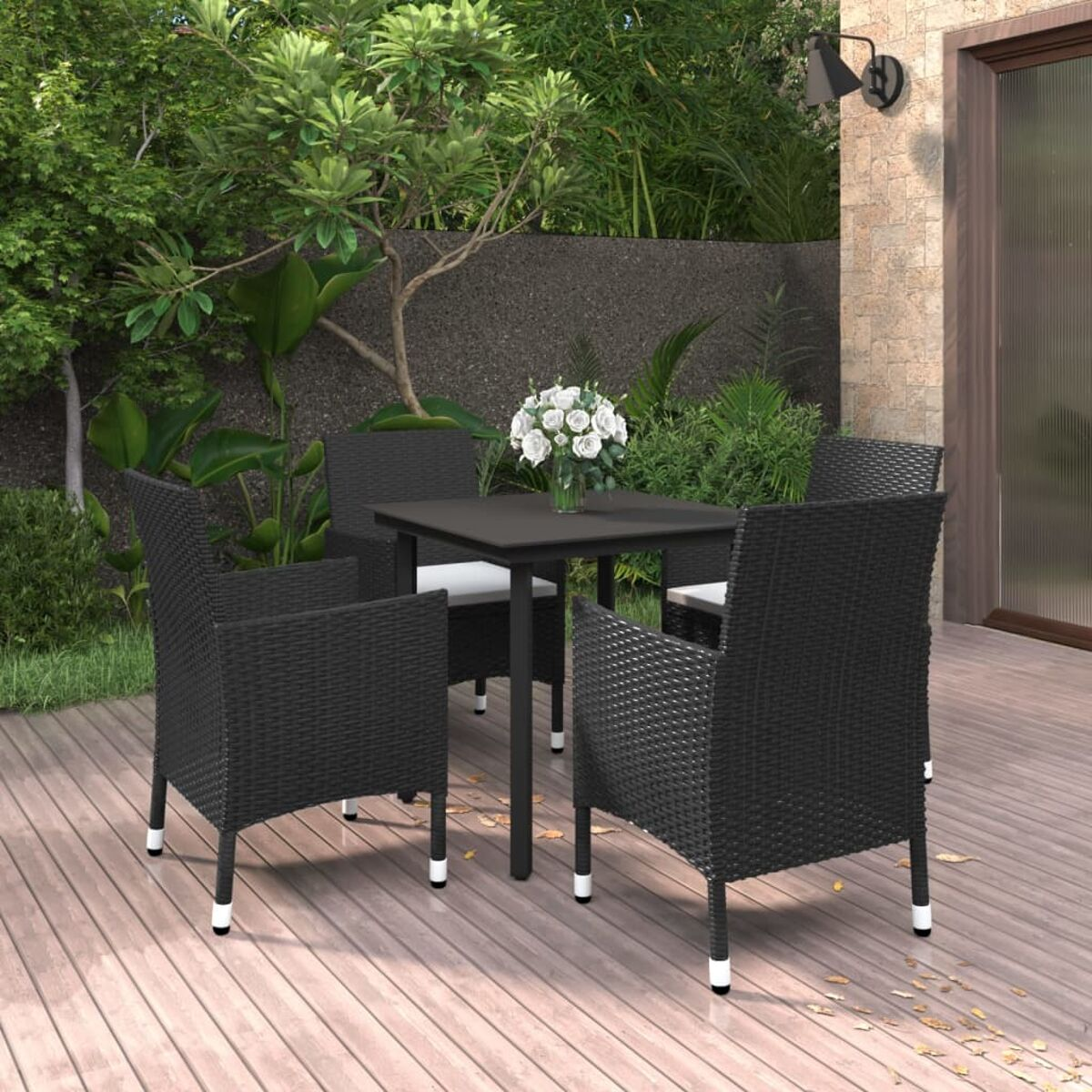Essgruppe für den Außenbereich mit schwarzen Stühlen und Tisch. Weiße Kissen, Blumen. Holzterrasse, Garten.