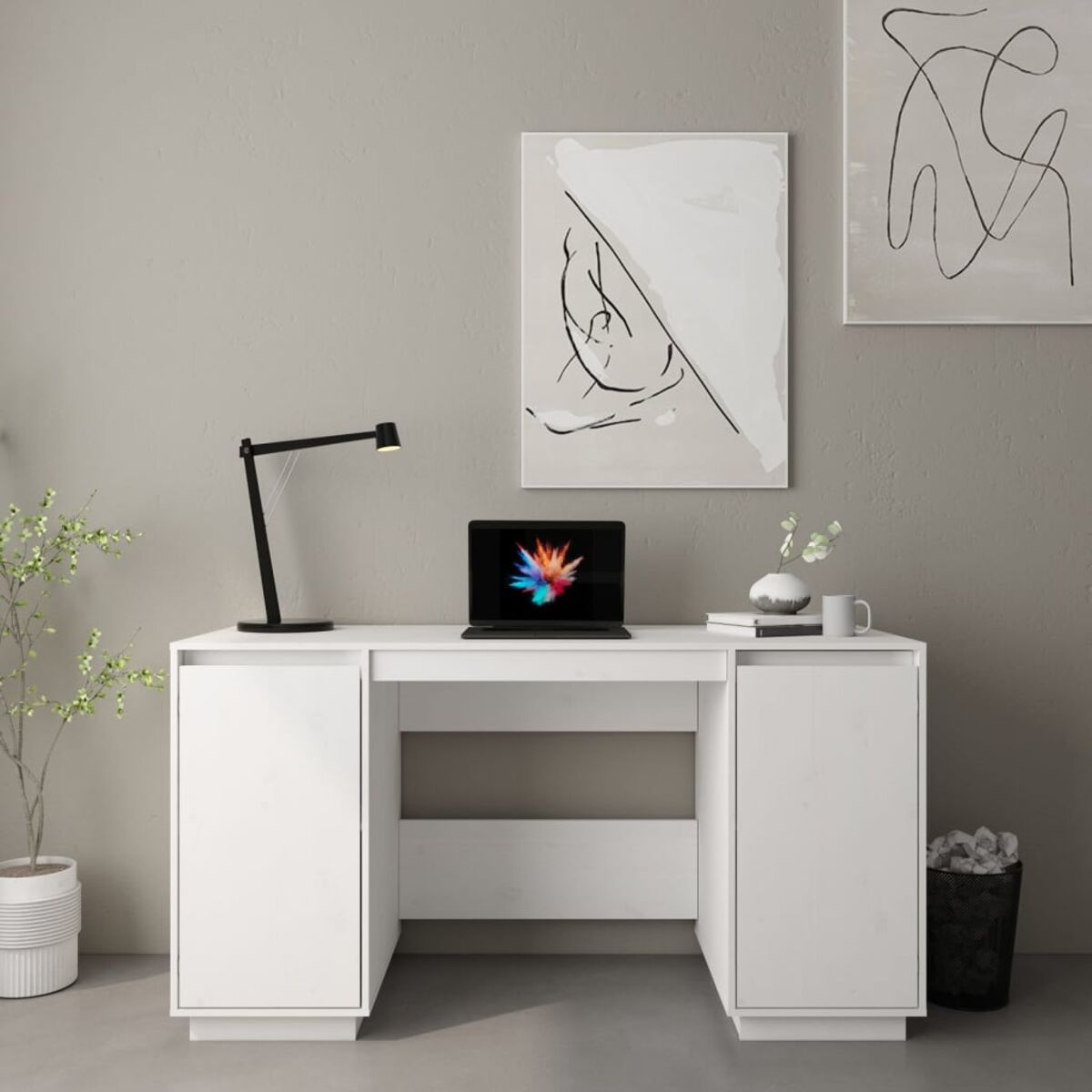 Ein weißer Schreibtisch mit Laptop, Lampe und Pflanze. Graue Wand im Hintergrund.