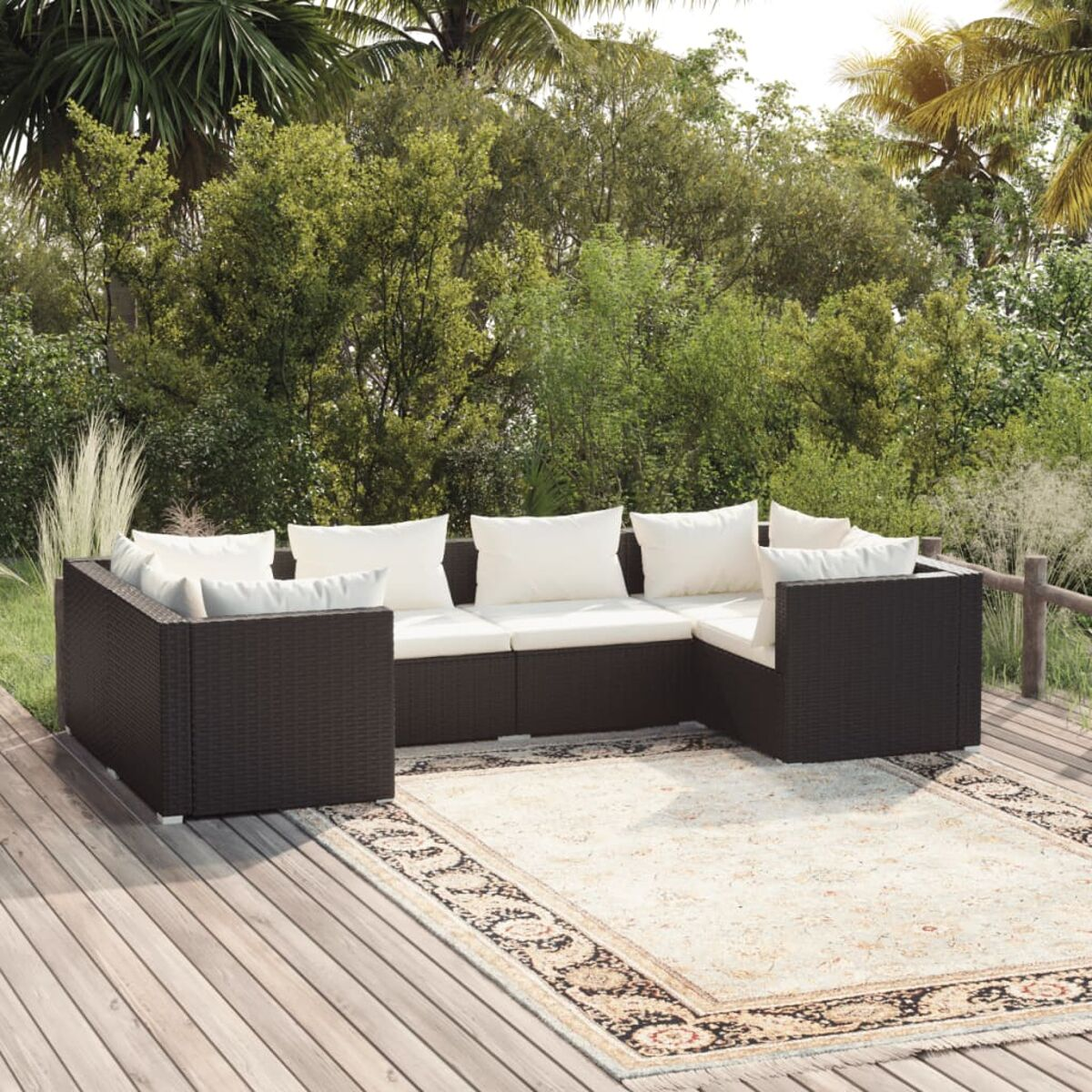 Outdoor-Sofa aus schwarzem Korbgeflecht mit weißen Kissen. Das Sofa steht auf einem Holzdeck mit Teppich, Bäume im Hintergrund.