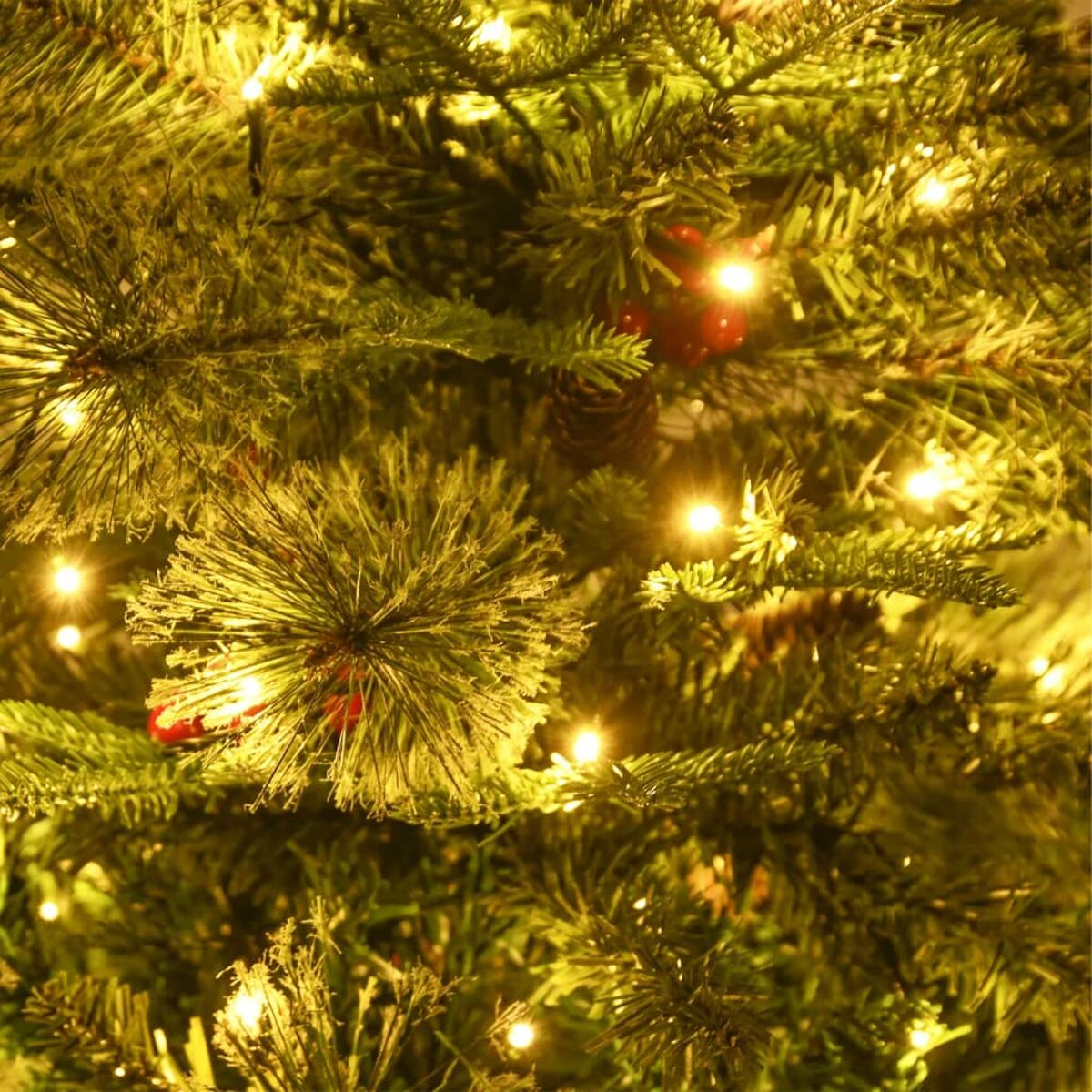 Nahaufnahme eines Weihnachtsbaums. Der Baum ist grün mit kleinen Lichtern, roten Beeren und braunen Tannenzapfen.
