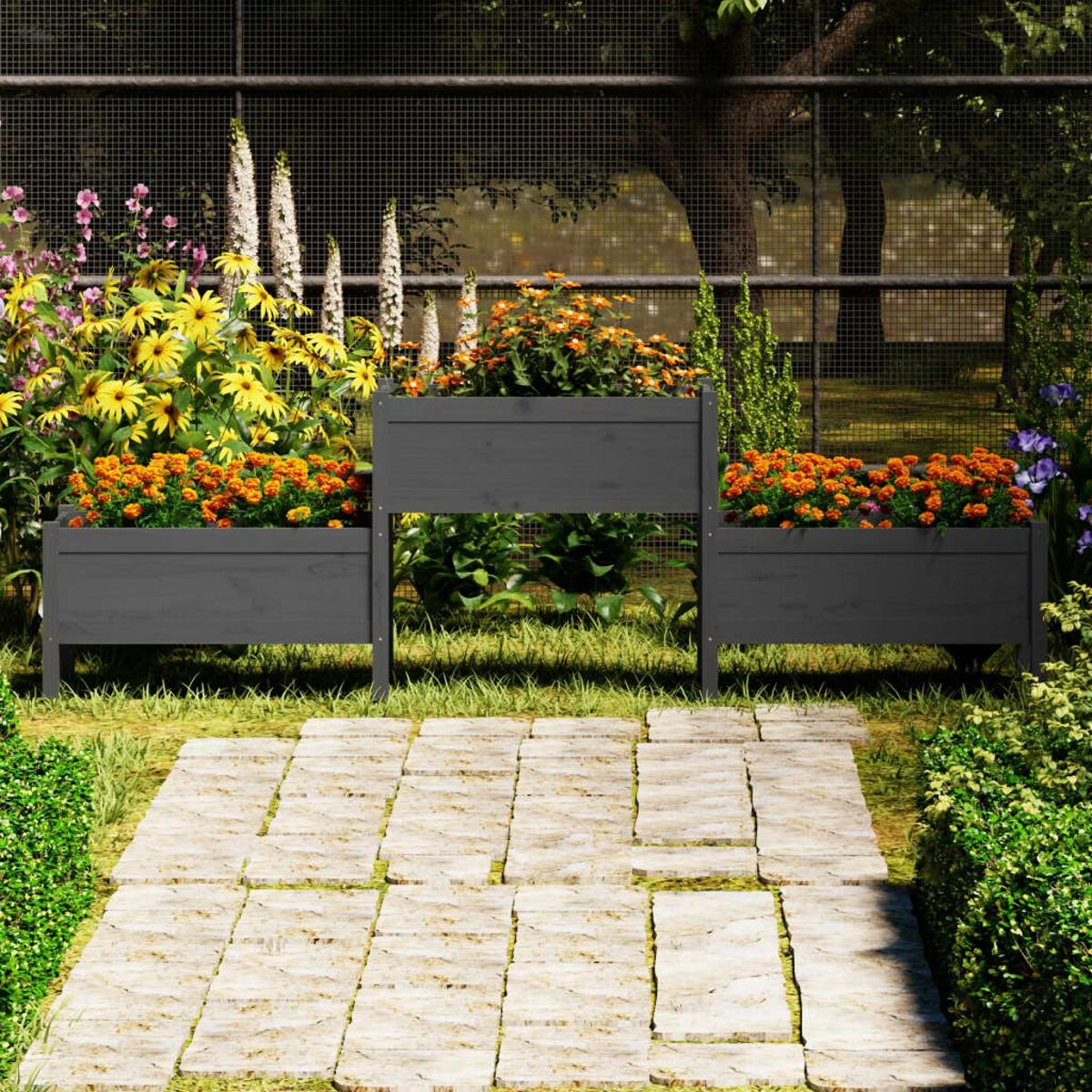 Blumenkästen mit Blumen auf einem Steinweg. Grüne Büsche und Metallzaun im Hintergrund.