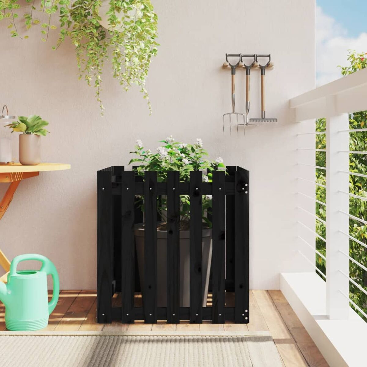 Schwarzer Pflanzkasten mit weißen Blumen, auf einem Balkon mit Werkzeugen.