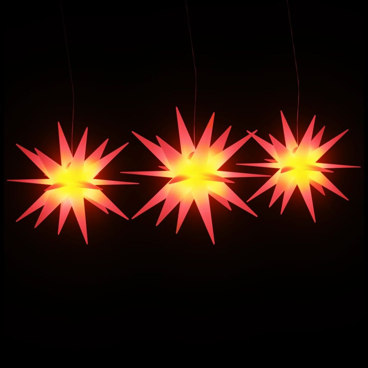 Drei sternförmige Lichter mit roten Rändern und gelben Zentren hängen auf schwarzem Hintergrund.