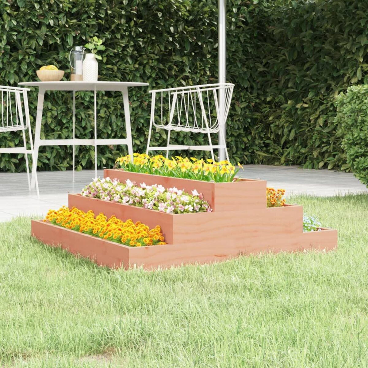 Gestuftes Gartenbeet mit Blumen. Weißer Tisch und Sonnenschirm im Hintergrund. Gras.