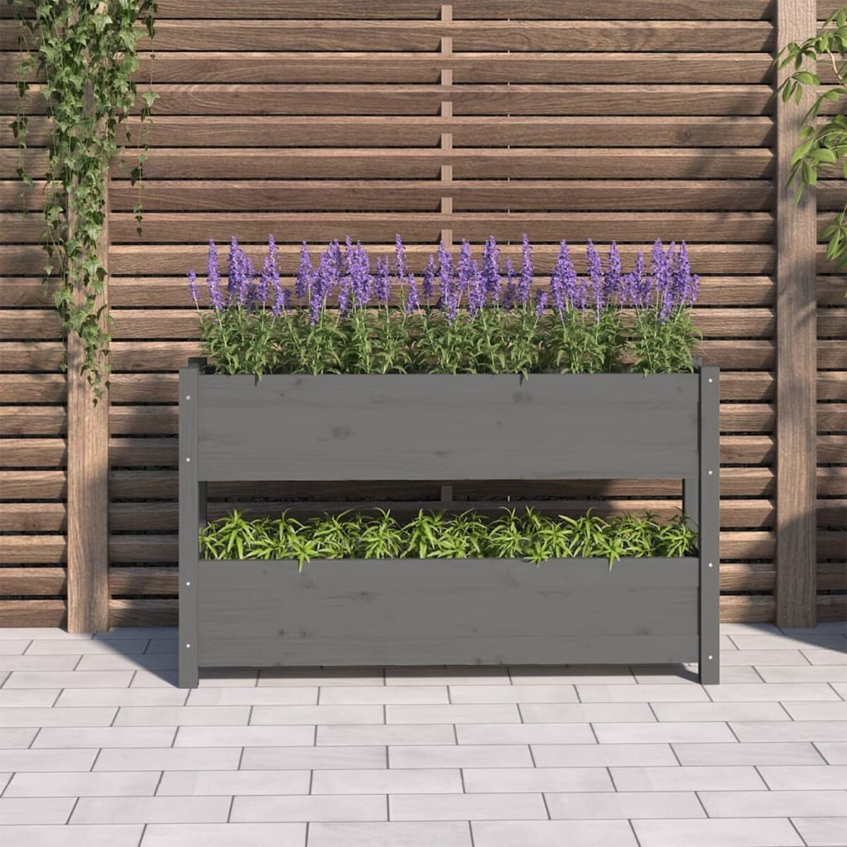 Grauer Holzpflanzer mit lila Blumen. Hintergrund: Holzzaun und Terrasse.