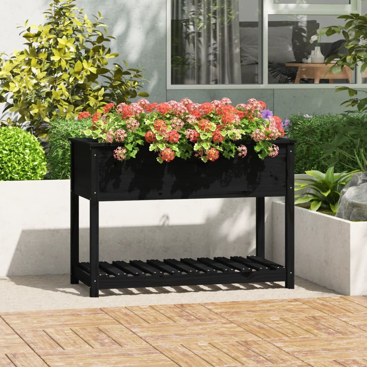 Schwarzer Gartenpflanzer aus Holz mit roten Blumen. Hat ein Regal darunter und steht auf einer Terrasse.