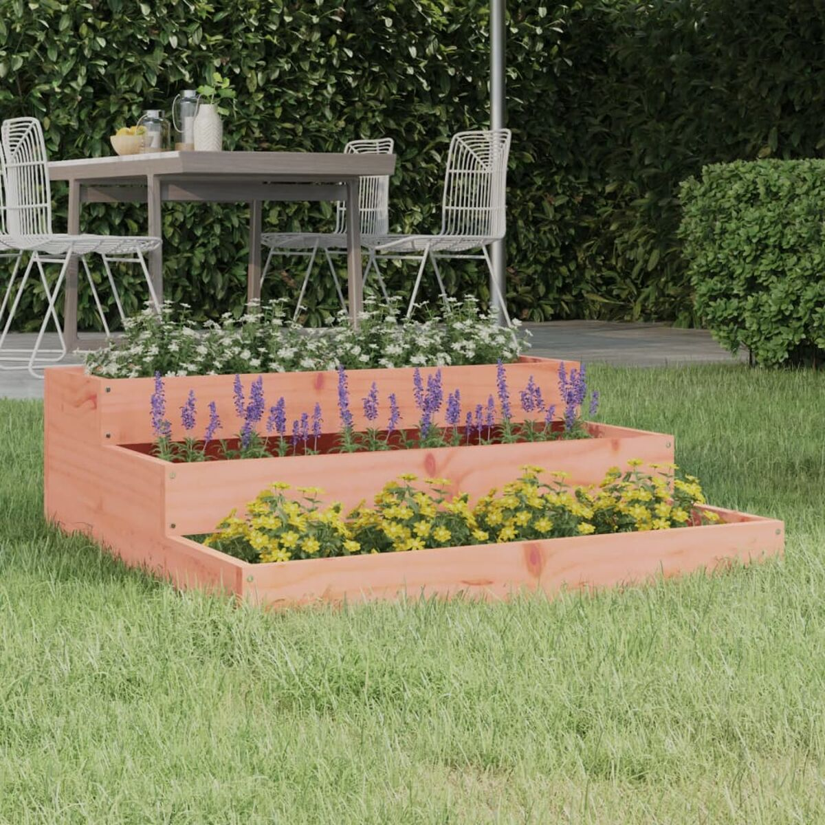 Ein mehrstufiger Holzpflanzer mit Blumen, auf Gras mit einem Tisch im Hintergrund.