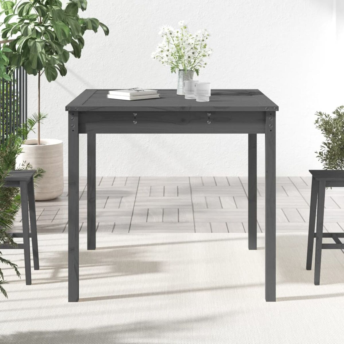 Grauer quadratischer Gartentisch mit weißer Oberfläche und Blumen. Zwei Stühle stehen daneben.