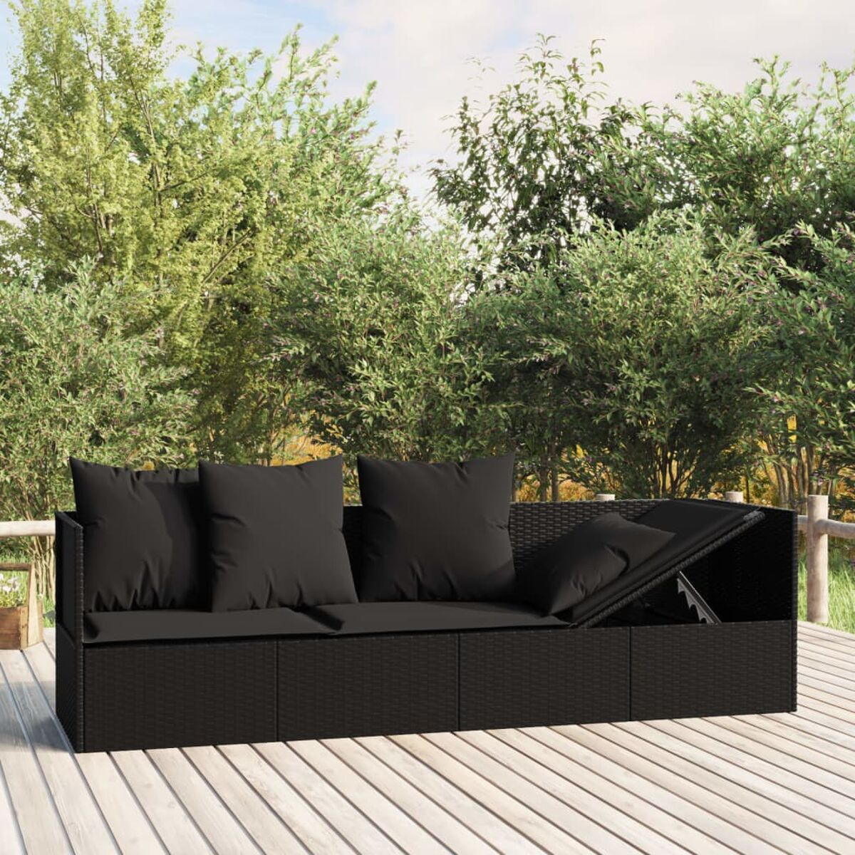 Schwarzes Korbmöbelsofa. Drei Kissen. Holzterrasse. Grüne Bäume im Hintergrund.