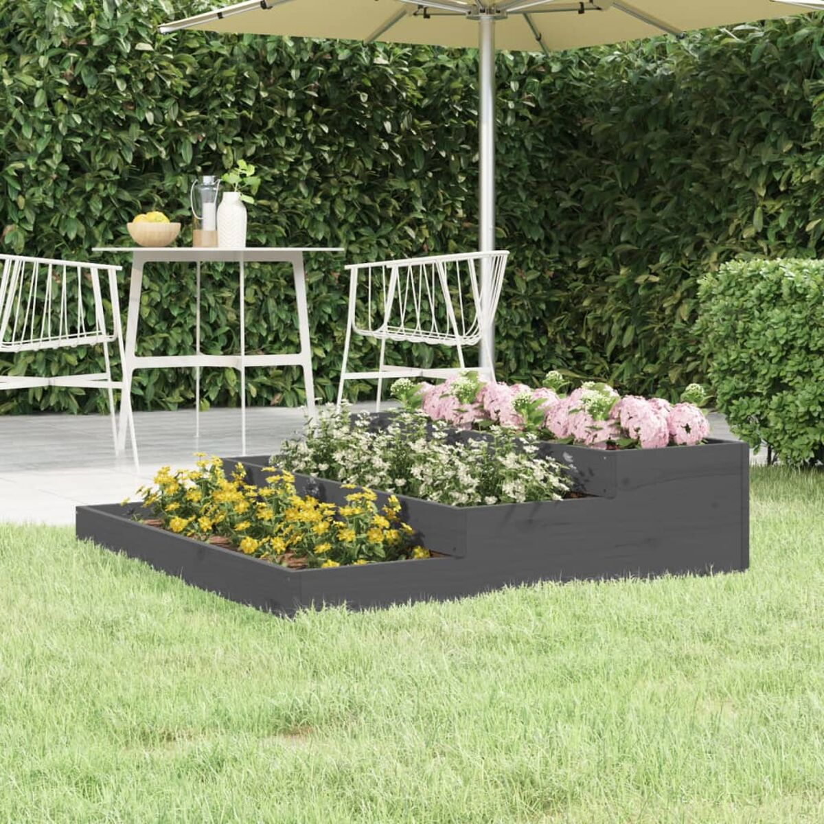 Gestufter Pflanzkasten mit Blumen und eine Terrassengarnitur in einem Garten.