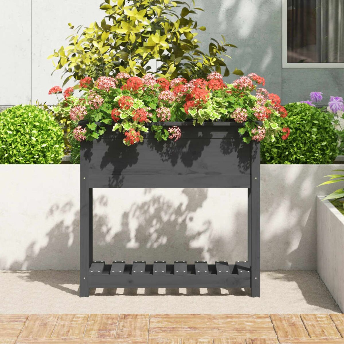 Schwarzer Pflanzkasten mit Blumen gefüllt. Graue Wand im Hintergrund.