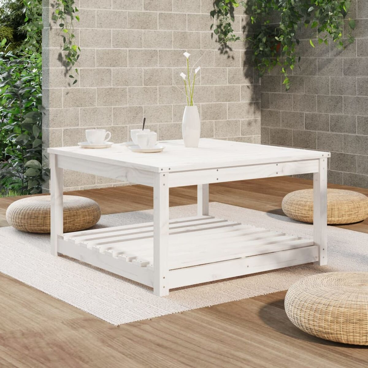 Weißer quadratischer Couchtisch auf einer Terrasse mit Pflanzen und Backsteinmauer im Hintergrund.