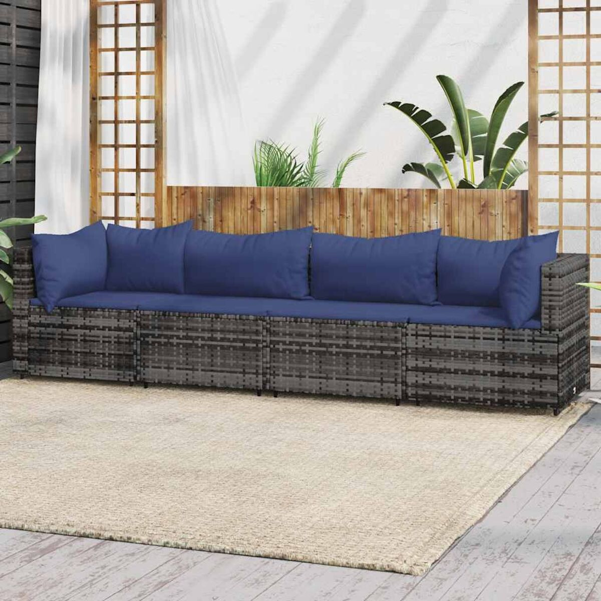 Rattansofa mit blauen Kissen auf beigem Teppich, mit Pflanzen im Hintergrund.