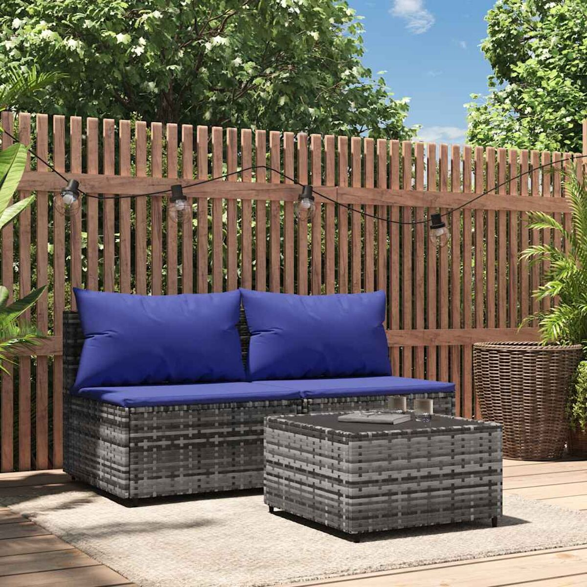 Graues Outdoor-Sofa aus Korbgeflecht mit blauen Kissen und einem Couchtisch. Hintergrund: Holzterrasse.