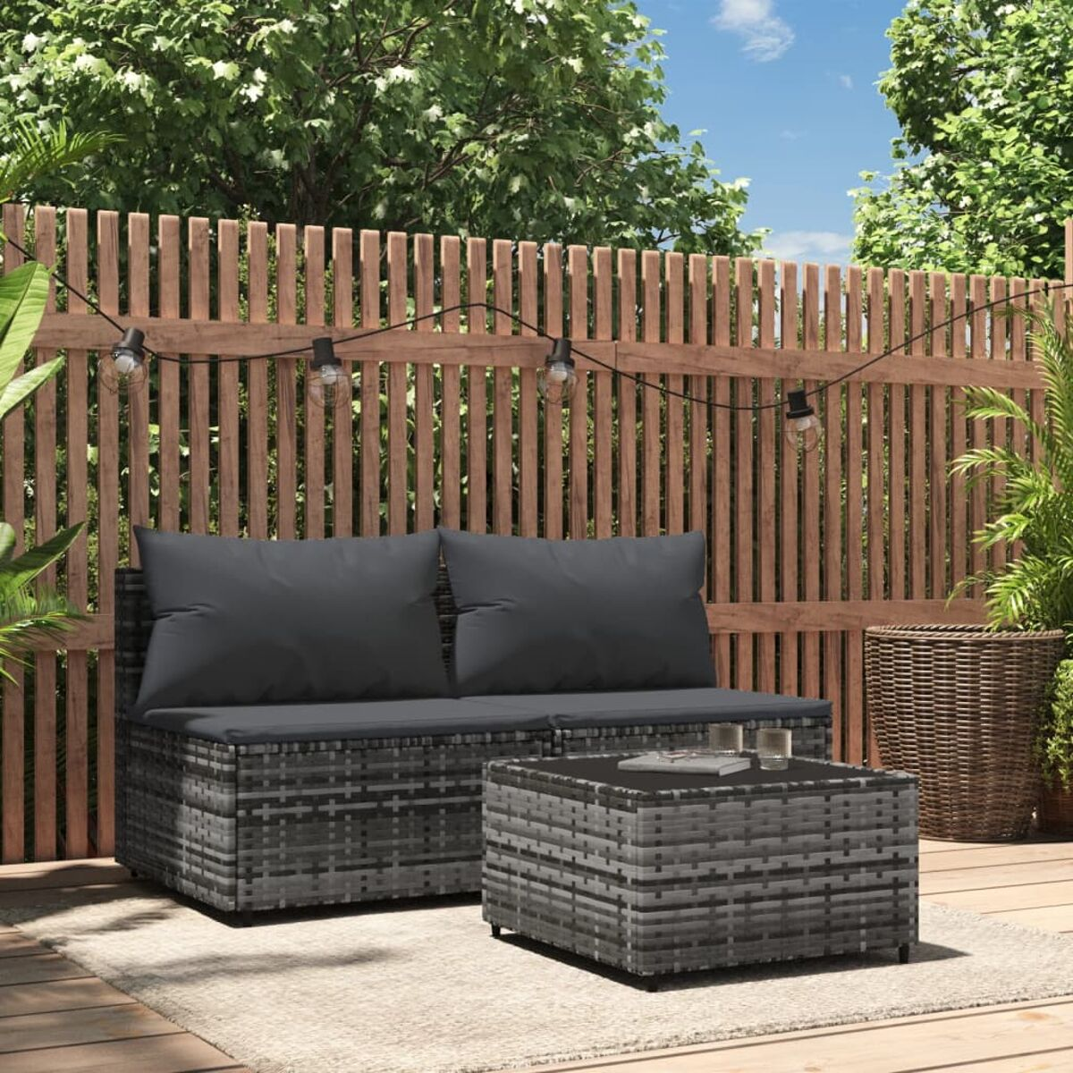 Rattan-Sofa und Tisch-Set im Freien, graue Kissen, Holzzaun im Hintergrund, Tageslicht.