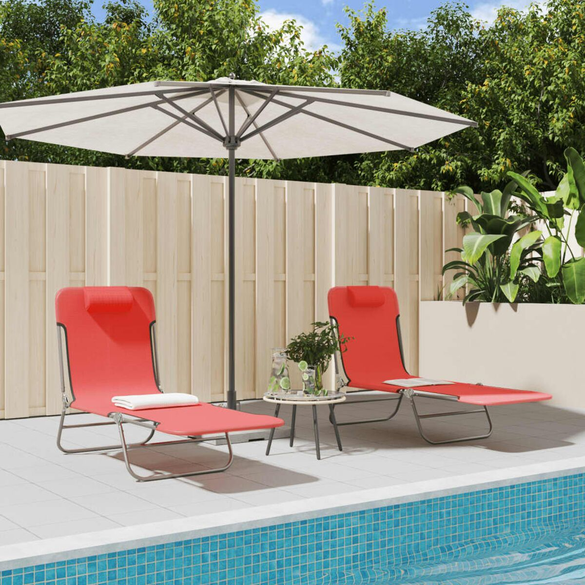 Zwei rote Liegestühle, Sonnenschirm, kleiner Tisch und ein Pool. Grüne Pflanzen und ein weißer Zaun im Hintergrund.