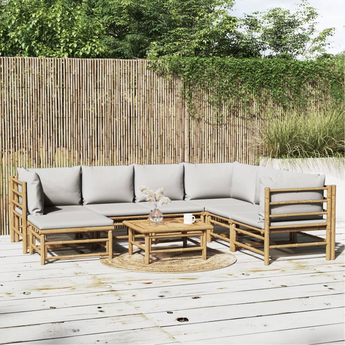 Ein Outdoor-Lounge-Set aus Bambus mit grauen Kissen. Ein kleiner Tisch steht mittig davor, im Hintergrund Bambuszäune.