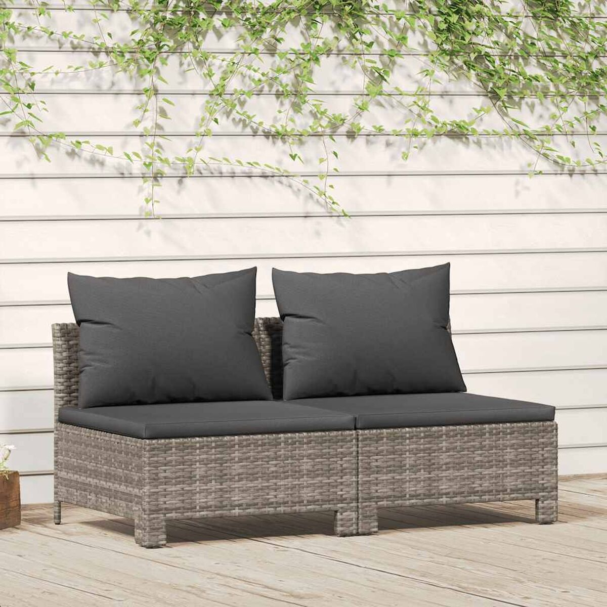 Graues Rattan-Zweisitzer-Sofa mit zwei grauen Kissen, auf einem Holzdeck mit Kletterpflanzen.