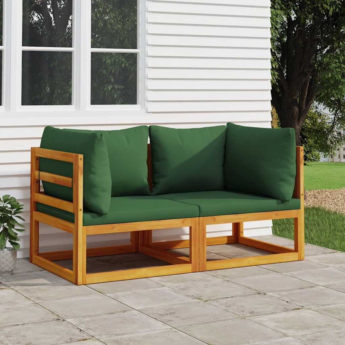 Outdoor-Sofa aus Holz mit grünen Kissen. Auf einer Terrasse platziert. Weißes Haus im Hintergrund sichtbar.