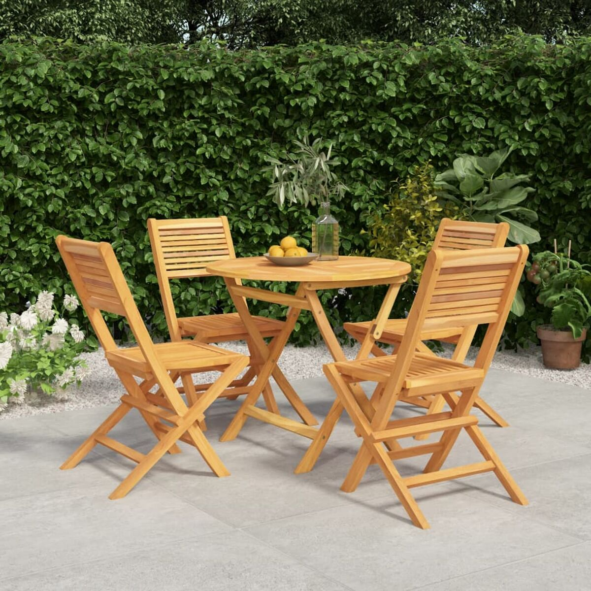 Ein Holztisch und vier Stühle stehen auf einer Terrasse. Dahinter befindet sich grünes Laub.