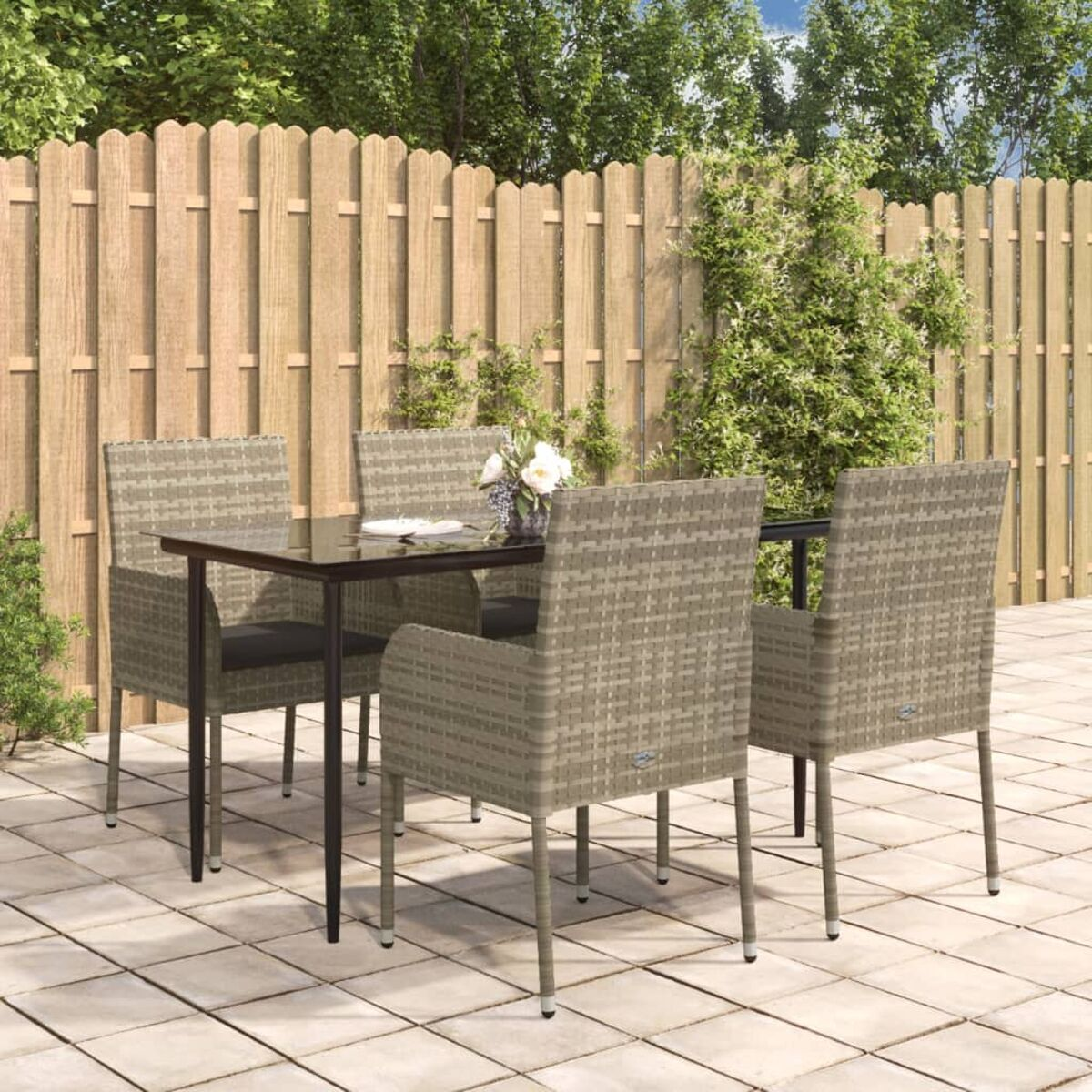 Eine Terrasse mit Tisch und Stühlen. Ein Holzzaun und Grünzeug im Hintergrund.