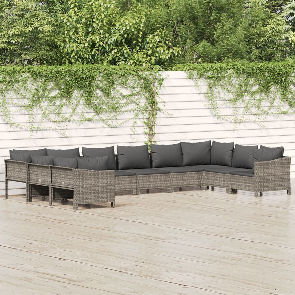 Graues Outdoor-Ecksofa aus Korbgeflecht mit dunkelgrauen Kissen auf einer Holzterrasse, mit weißem Zaun.