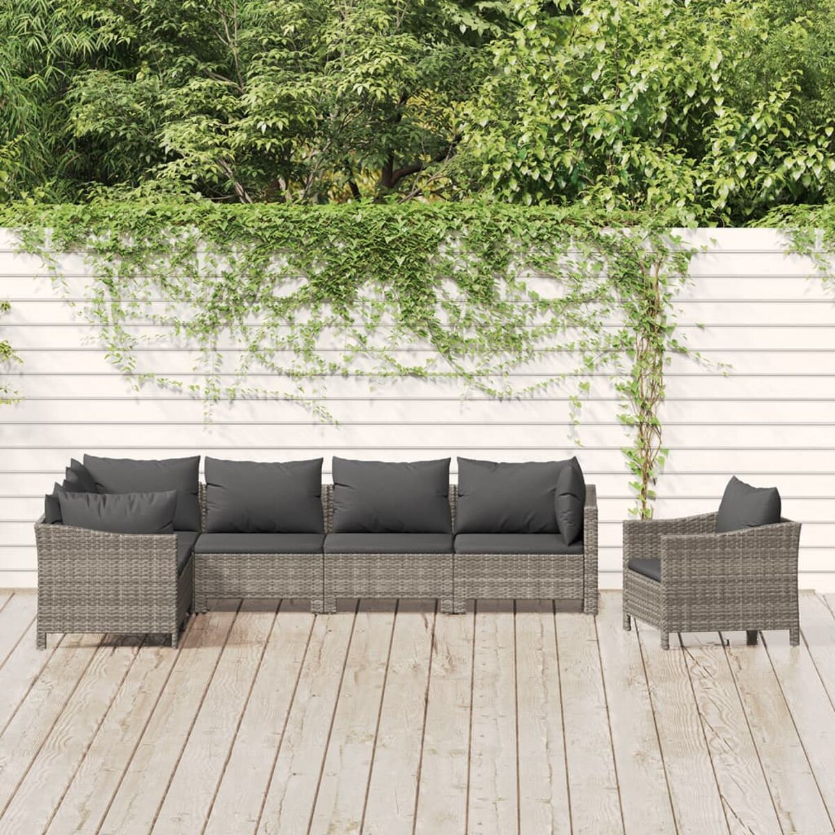 Graues Outdoor-Geflechtmöbel-Set auf einem Holzdeck, mit weißem Zaun und Grün-Hintergrund.
