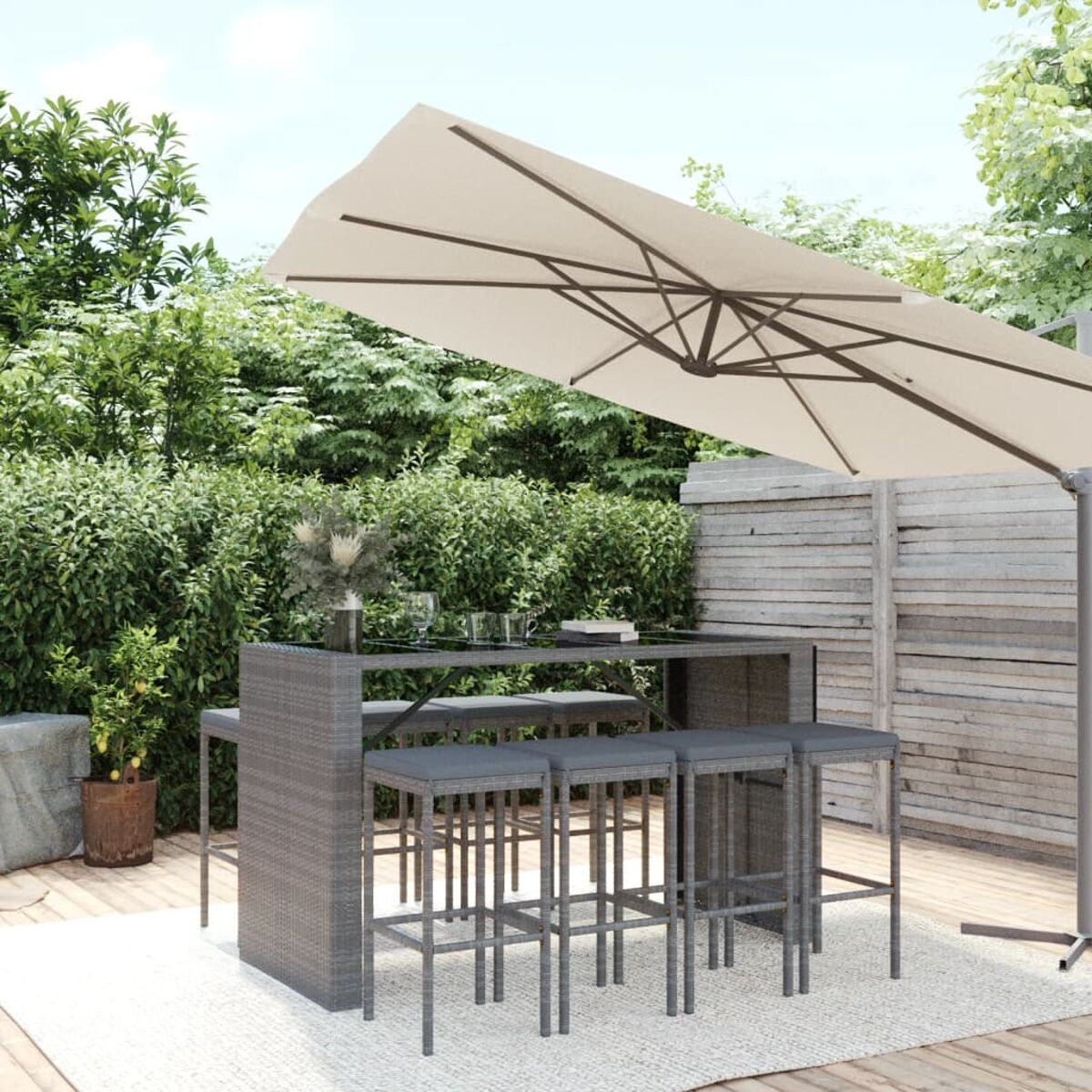 Outdoor-Bartisch-Set mit Tisch, vier Hockern und einem Sonnenschirm. Grüne Büsche im Hintergrund.