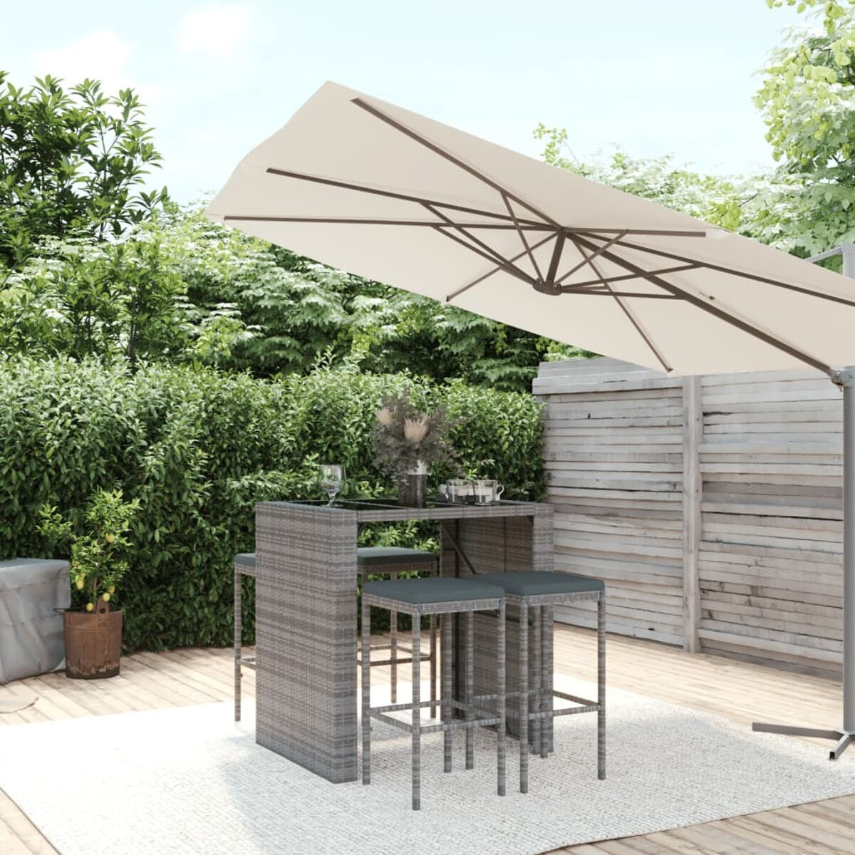 Outdoor-Essgruppe mit grauem Korbgeflecht, beigem Schirm und grünem Hintergrund. Tisch, Hocker und Grün.