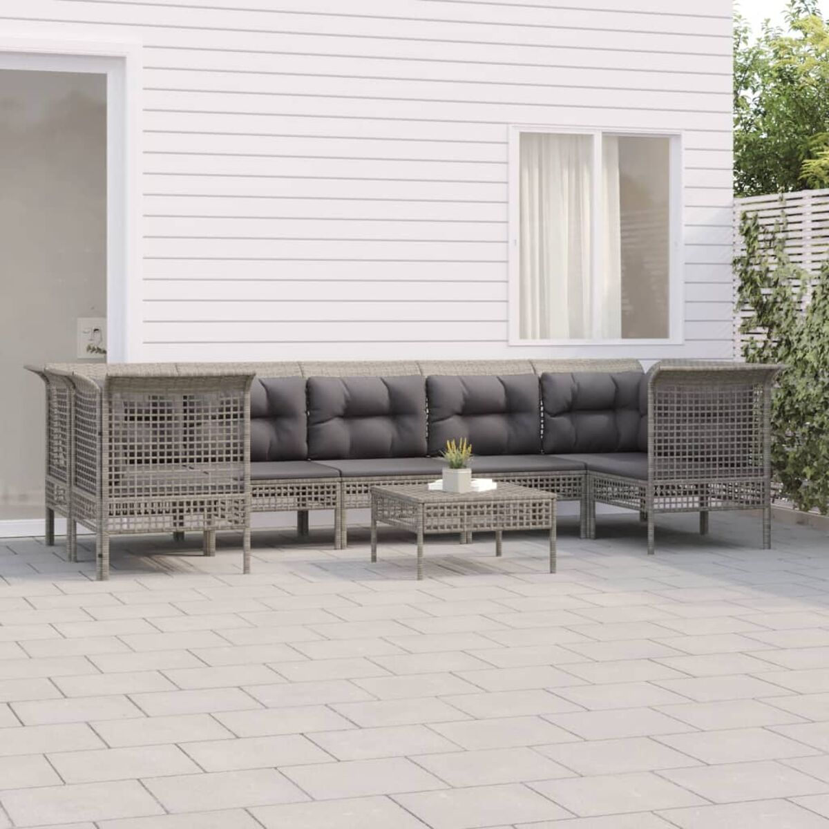 Graues Outdoor-Geflechtmöbel-Set mit Kissen, Tisch und Pflanzen.