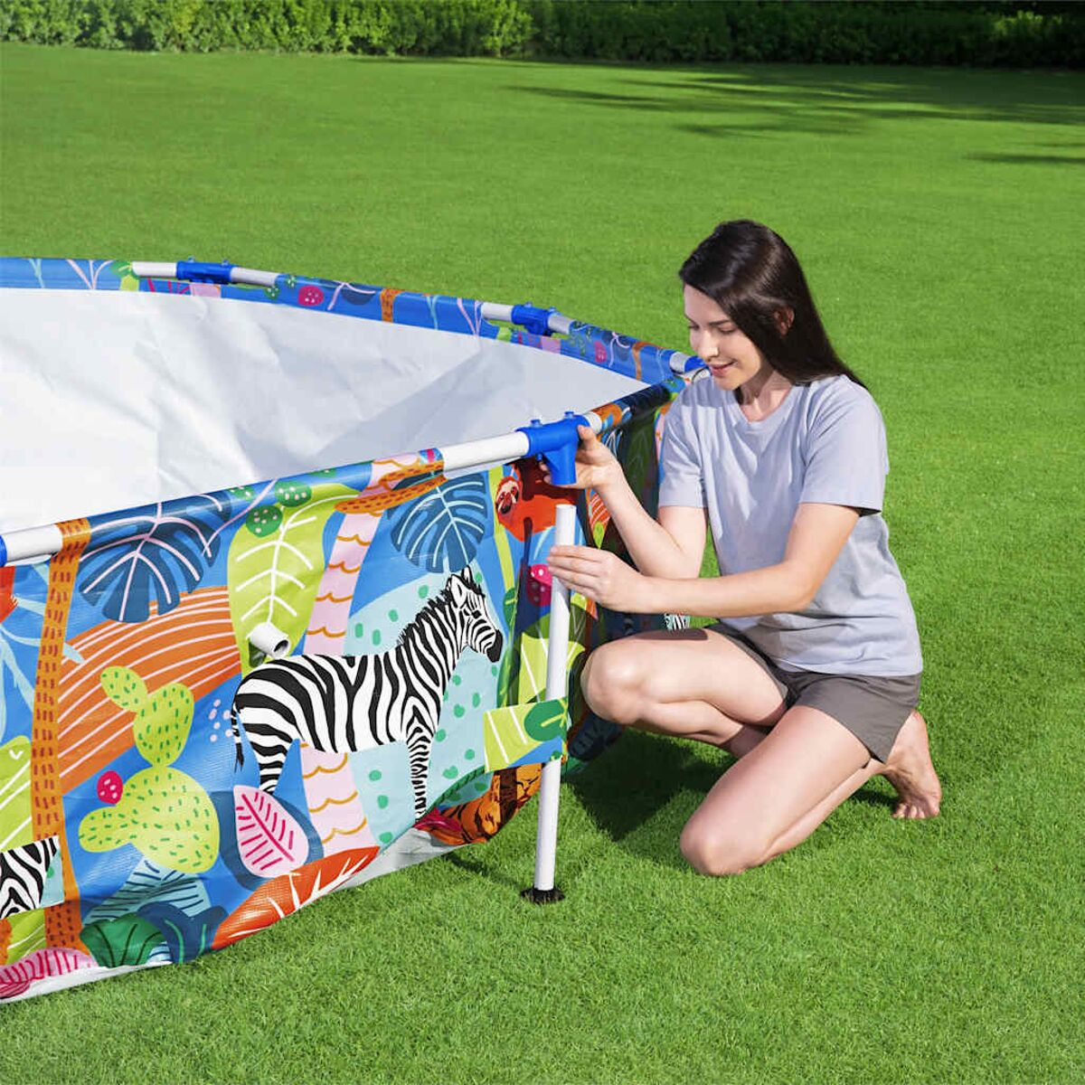 Eine Frau in Shorts kniet an einem Pool und richtet die Seite ein. Ein Zebra ist auf dem Pool.