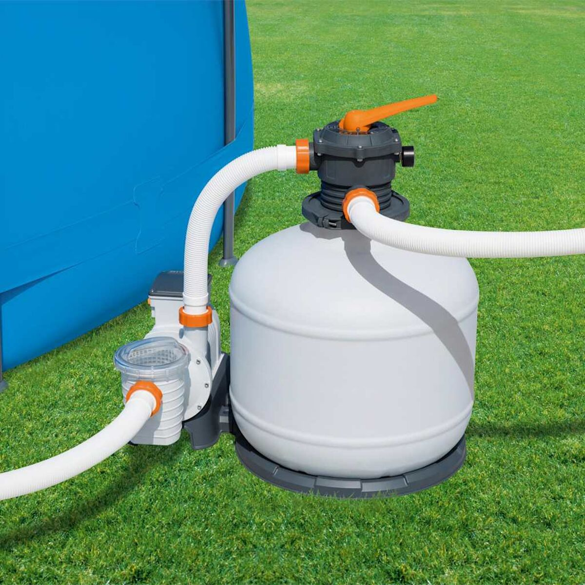 Poolfiltersystem mit weißem Tank, Schläuchen und einem orangen Griff auf einer grünen Wiese.