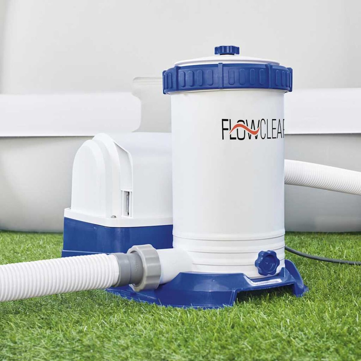 Weißer und blauer Poolfilter mit Schläuchen, auf grünem Gras. Weißer Hintergrund.