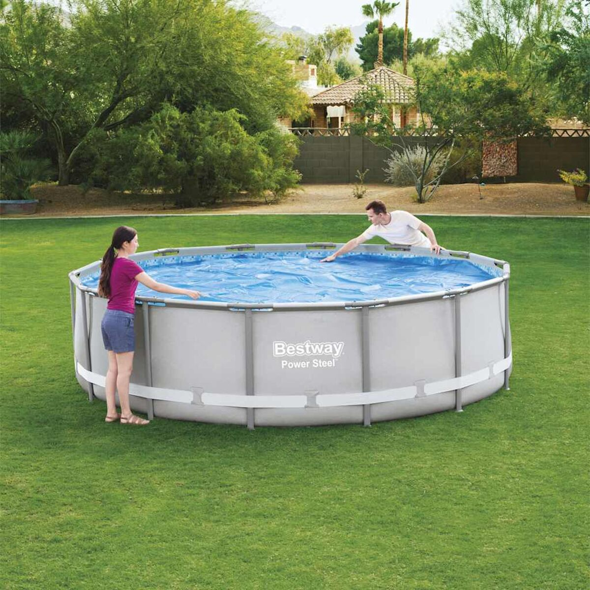 Zwei Personen in der Nähe eines großen, runden Pools. Der Pool ist mit Wasser gefüllt und von Gras umgeben.