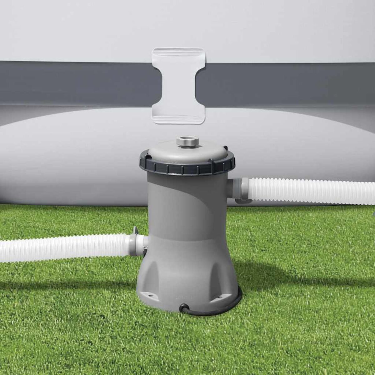 Ein graues Poolfiltersystem auf grünem Gras. Weiße Schläuche sind angeschlossen. Ein weißer Pool im Hintergrund.