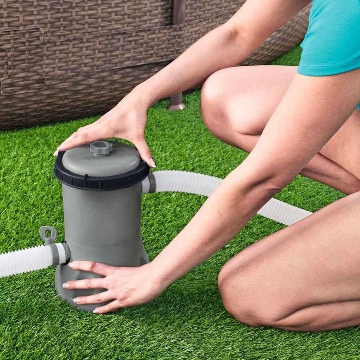 Hände einer Person, die mit einem grauen Poolfilter arbeiten, auf grünem Gras.