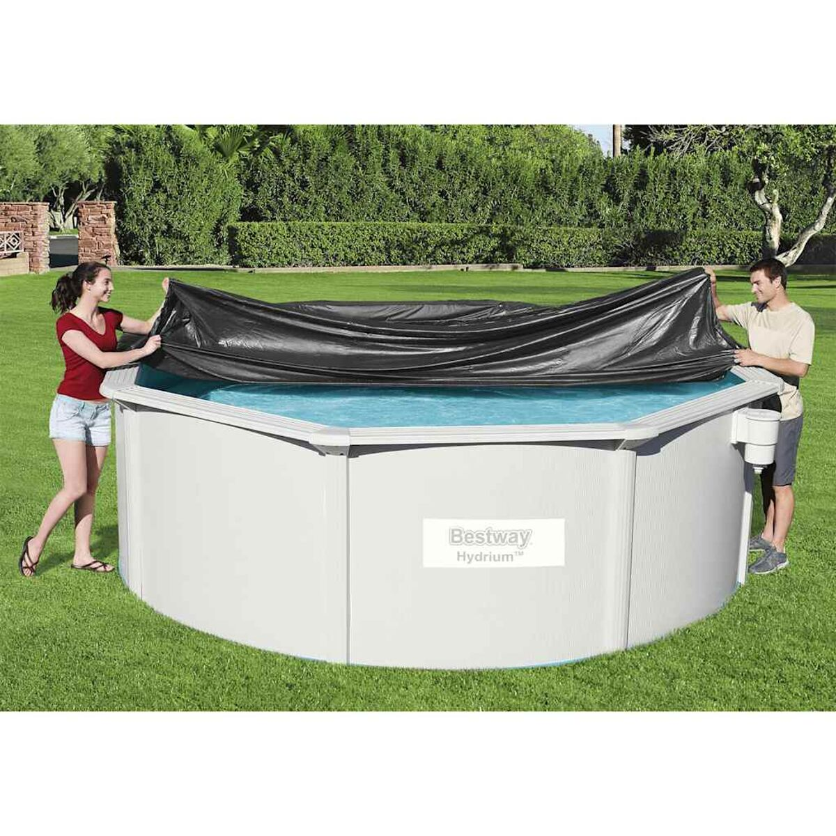 Zwei Personen bedecken einen blauen oberirdischen Pool mit einer schwarzen Abdeckung in einer Wiese.