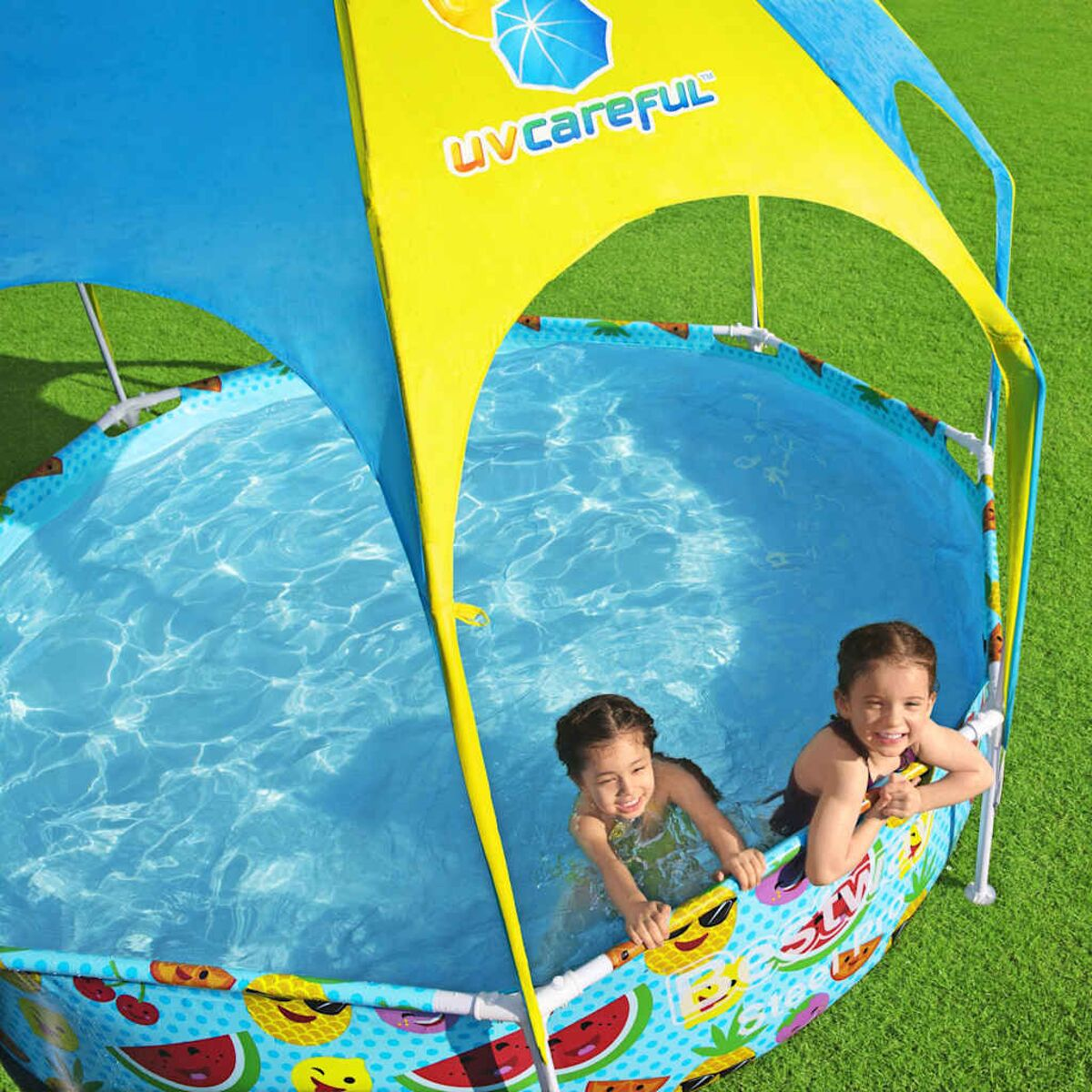 Zwei Mädchen in einem Pool unter einem blau-gelben Baldachin. Der Pool hat Fruchtdrucke.