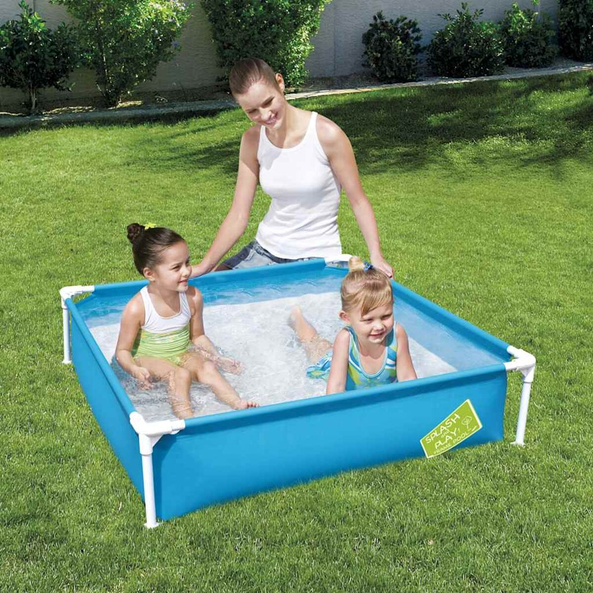 Ein kleiner blauer rechteckiger Pool mit drei Kindern und einer Frau, im Garten.