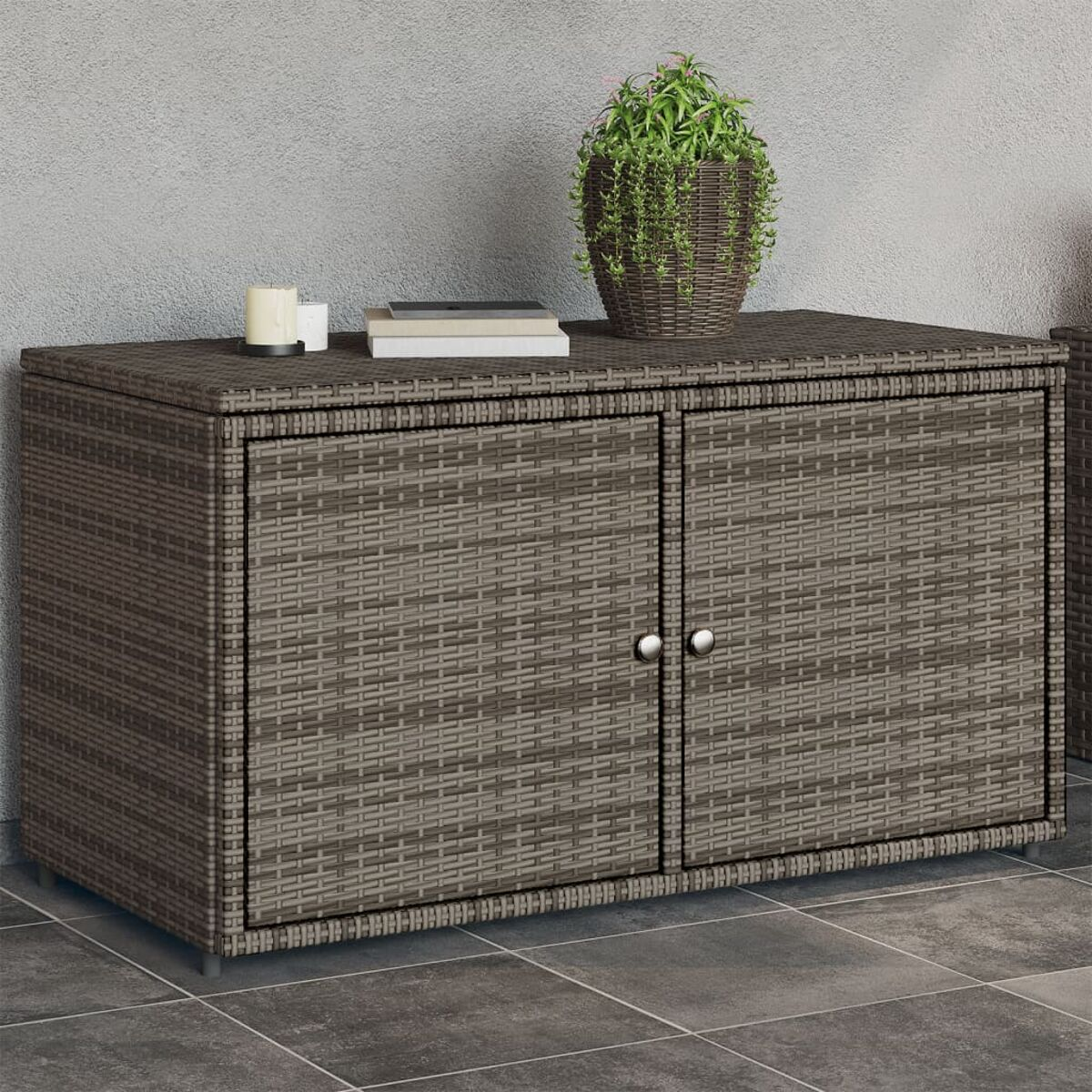 Korb-Schrank mit zwei Türen. Obenauf eine Pflanze und Kerzen. Gegen eine graue Wand gestellt.