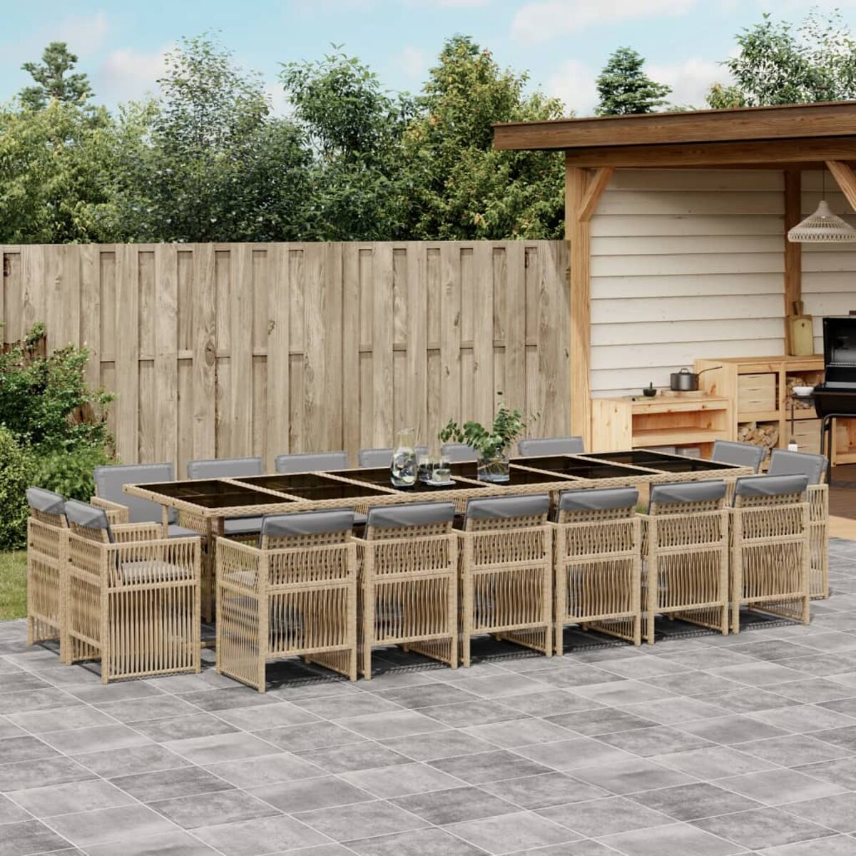 Set da pranzo all'aperto con tavolo e sedie su un patio pavimentato. Recinzione in legno e alberi sullo sfondo.
