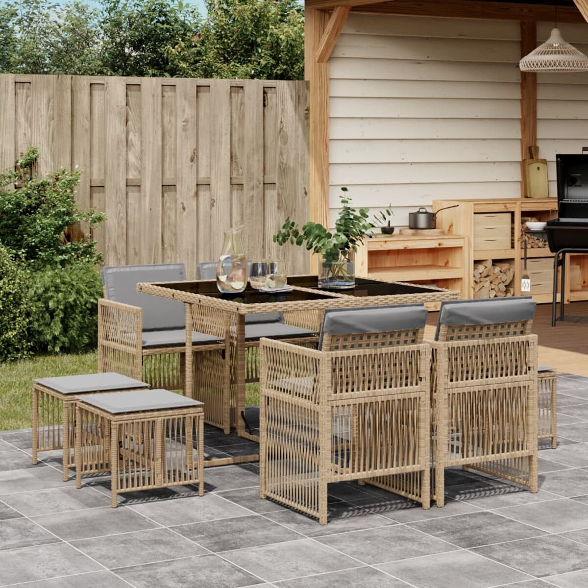 Set da pranzo da patio con tavolo e sedie. Su un patio in pietra. Vimini beige e cuscini grigi.
