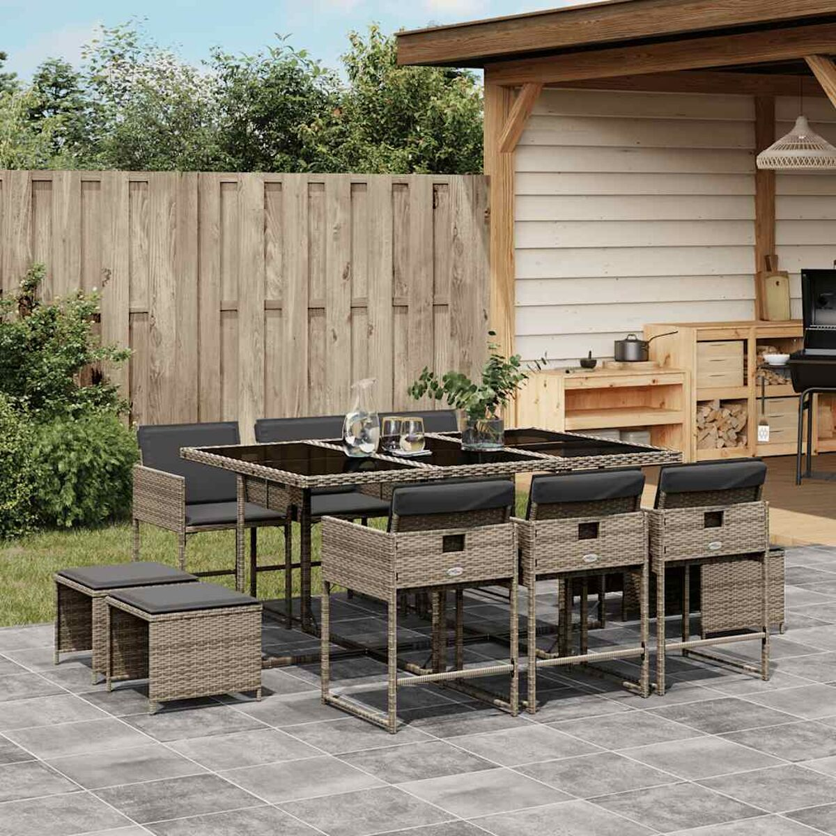 Set da pranzo per patio con tavolo e sedie. Cornici in legno e cuscini grigi. Sfondo: cortile e cielo.