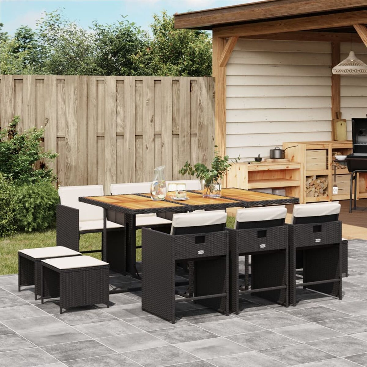 Essgruppe im Freien: Tisch, Stühle, Hocker. Holztisch, schwarze Korbstühle und Hocker. Beige Kissen.