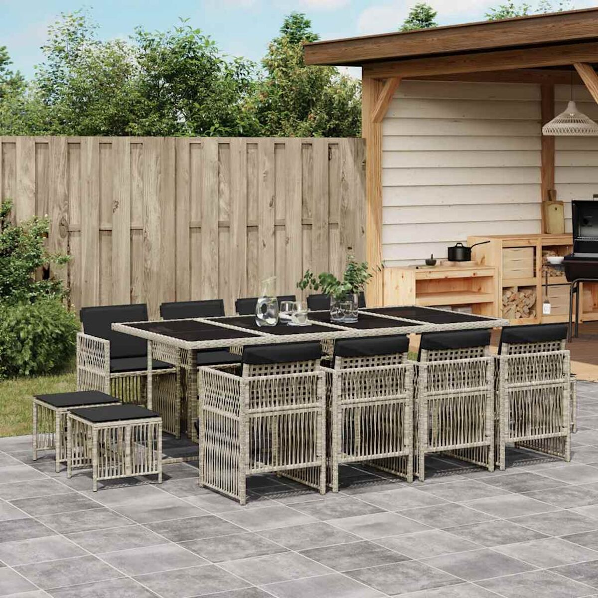 Set da pranzo all'aperto con cuscini neri. Patio con struttura in legno e piante.