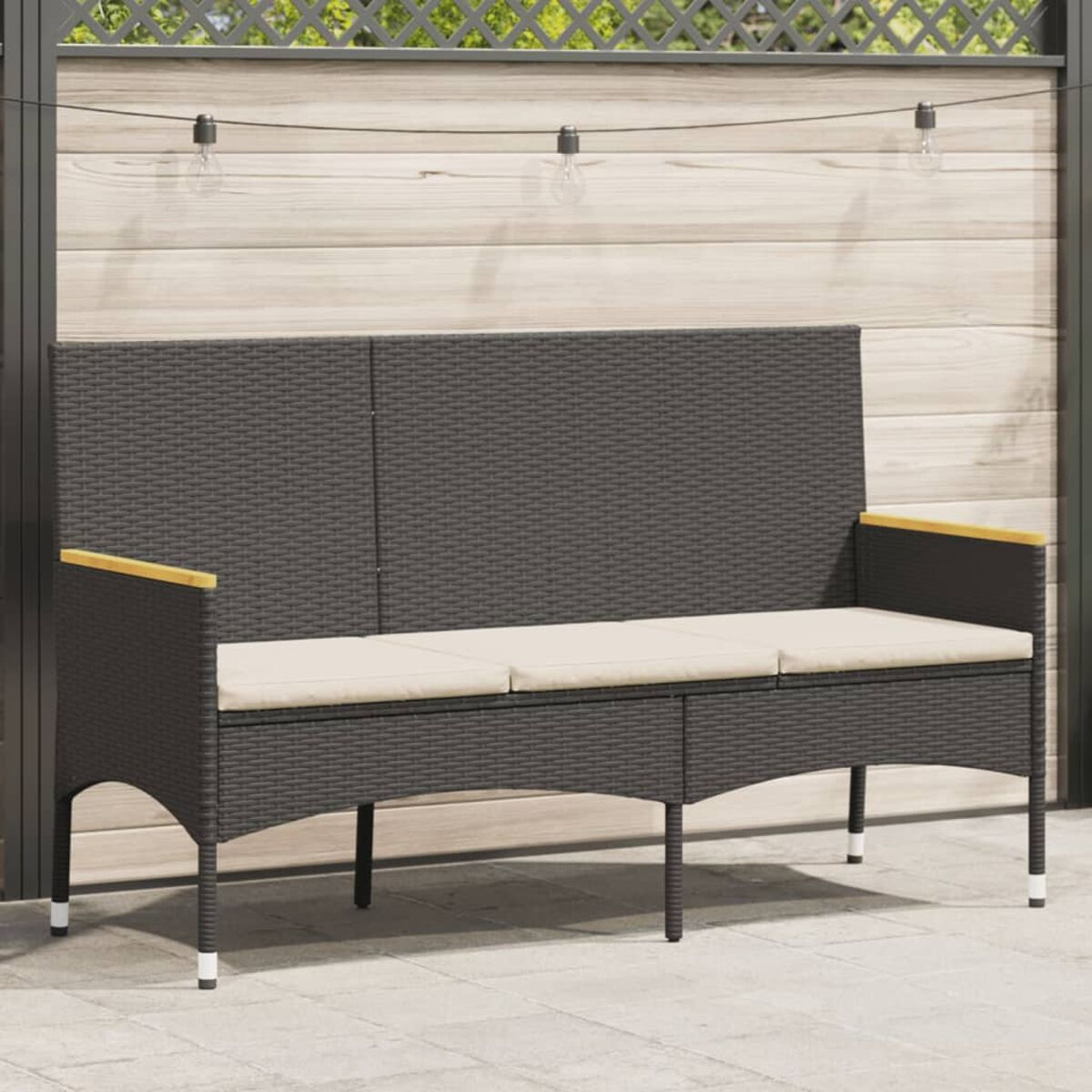 Una panca in rattan grigio scuro con un cuscino bianco. Ha braccioli in legno ed è accanto a una recinzione in legno.