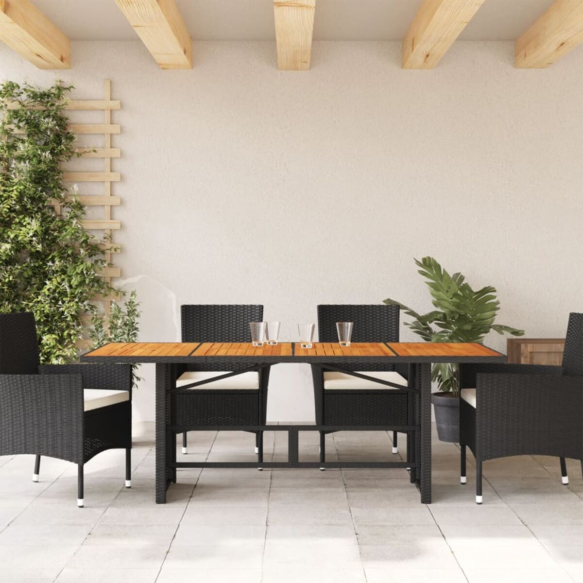 Set da pranzo all'aperto: tavolo, quattro sedie, bicchieri e piante in un patio soleggiato.