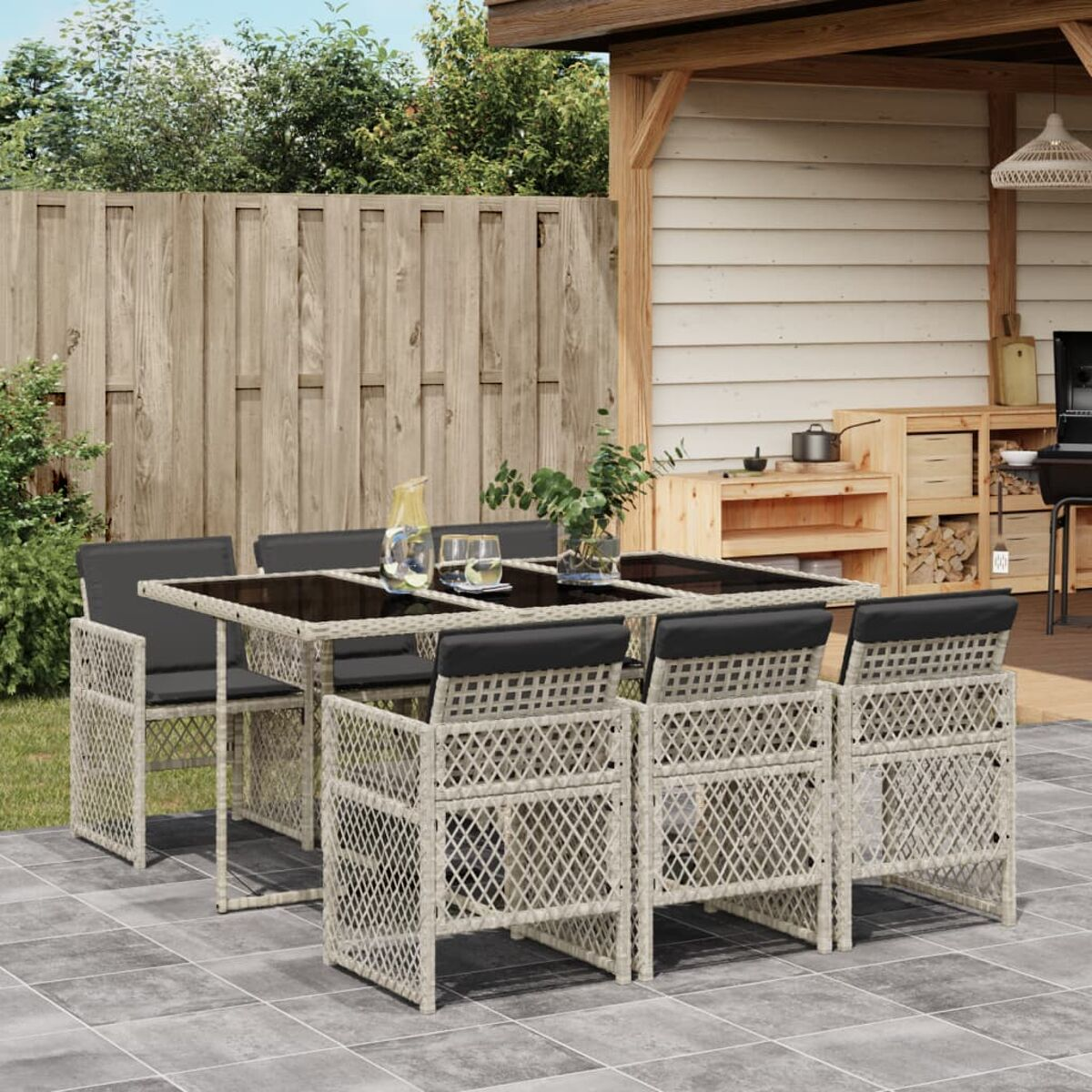 Set da patio con tavolo, sedie e bevande. Vimini beige con cuscini neri, su un patio in pietra.