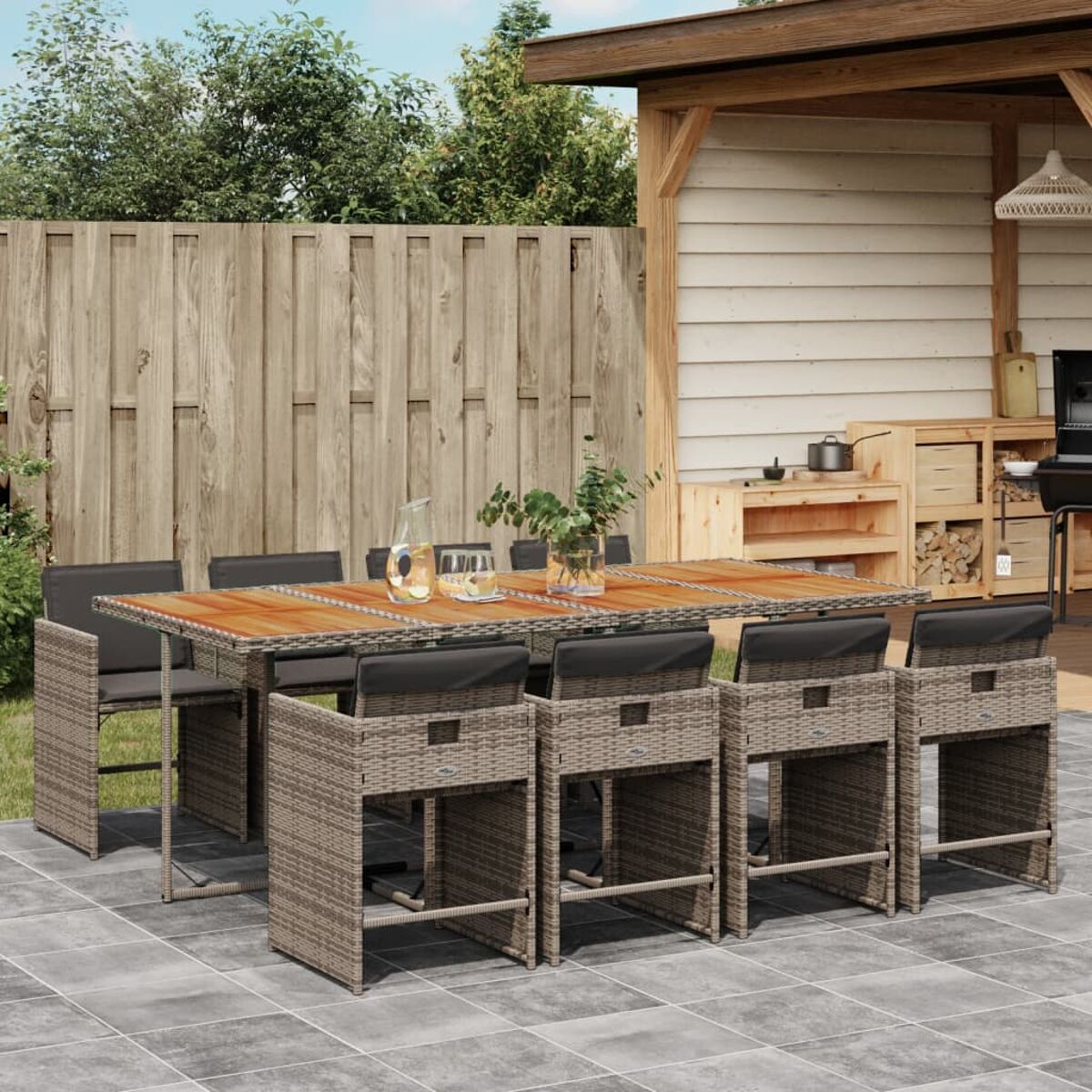 Essgruppe im Freien mit Tisch und Barhockern. Der Tisch hat eine Holzplatte und schwarze Kissen.